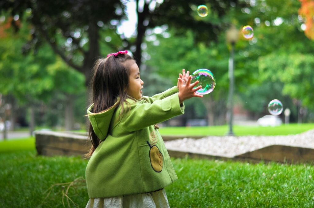 a little girl playing outside reaches for a bubble with a smile on her face, showing the power of play therapy in new jersey