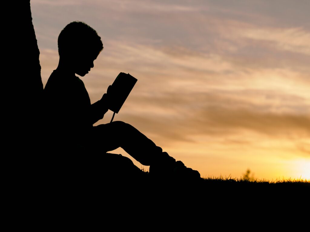 child reading a book sitting against a tree having a hard time navigating the school year transition