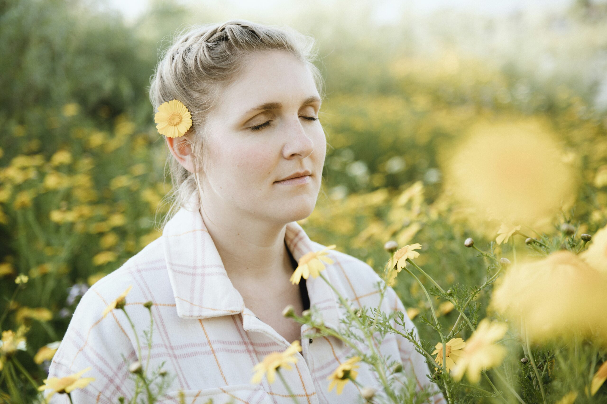 a woman with her eyes closed in a flower field practicing self-compassion